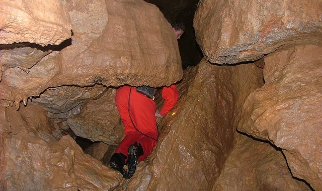 Caver squeezes through a tight gap in a pothole