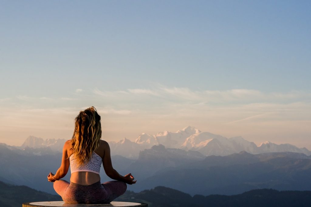 Woman sitting meditating on the top of a mountain